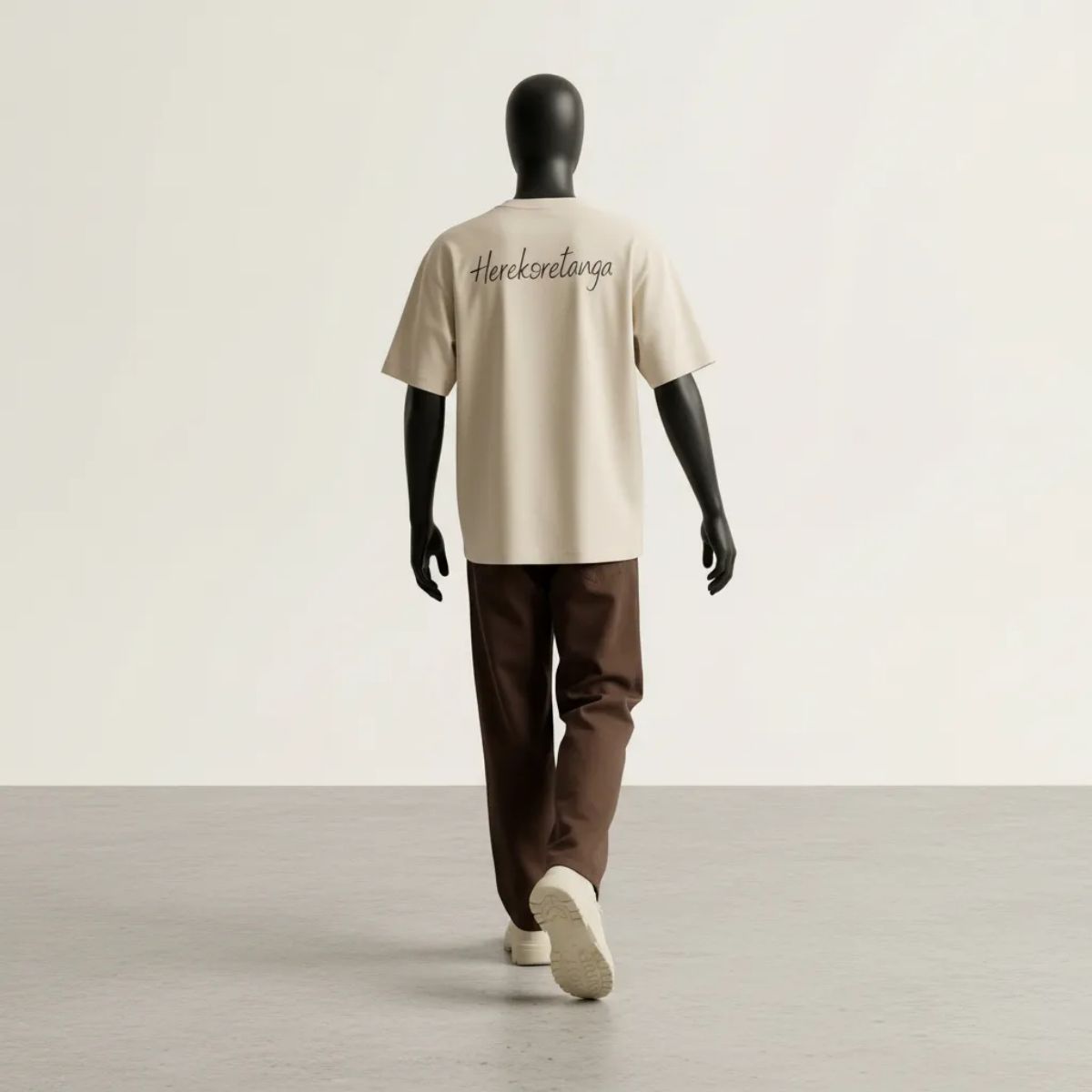 Dinamismo strutturale: visione posteriore in movimento del Modulo Herekoretanga. Il jersey pesante color sabbia sostiene il volume moto-boxy, proiettando il rigore del design GL MANIFACTORY in una dimensione urbana ispirata alla forza e alla resilienza della cultura Maori.