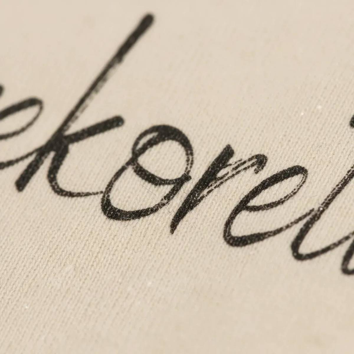 Close-up della stampa calligrafica "Herekoretanga" su tessuto Heavy Jersey sabbia. Il dettaglio mostra l'integrazione tra l'inchiostro e la fibra di cotone biologico da 240g, un tributo di GL MANIFACTORY alla forza espressiva e al simbolismo della cultura Maori