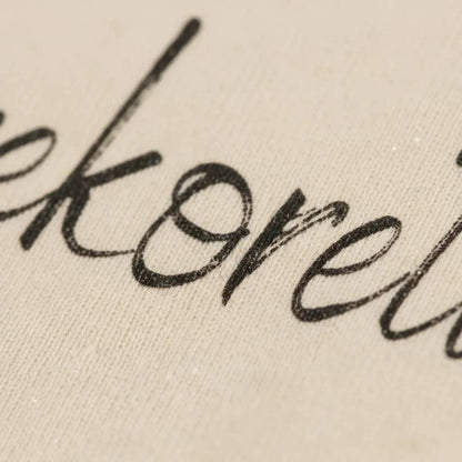 Close-up della stampa calligrafica "Herekoretanga" su tessuto Heavy Jersey sabbia. Il dettaglio mostra l'integrazione tra l'inchiostro e la fibra di cotone biologico da 240g, un tributo di GL MANIFACTORY alla forza espressiva e al simbolismo della cultura Maori