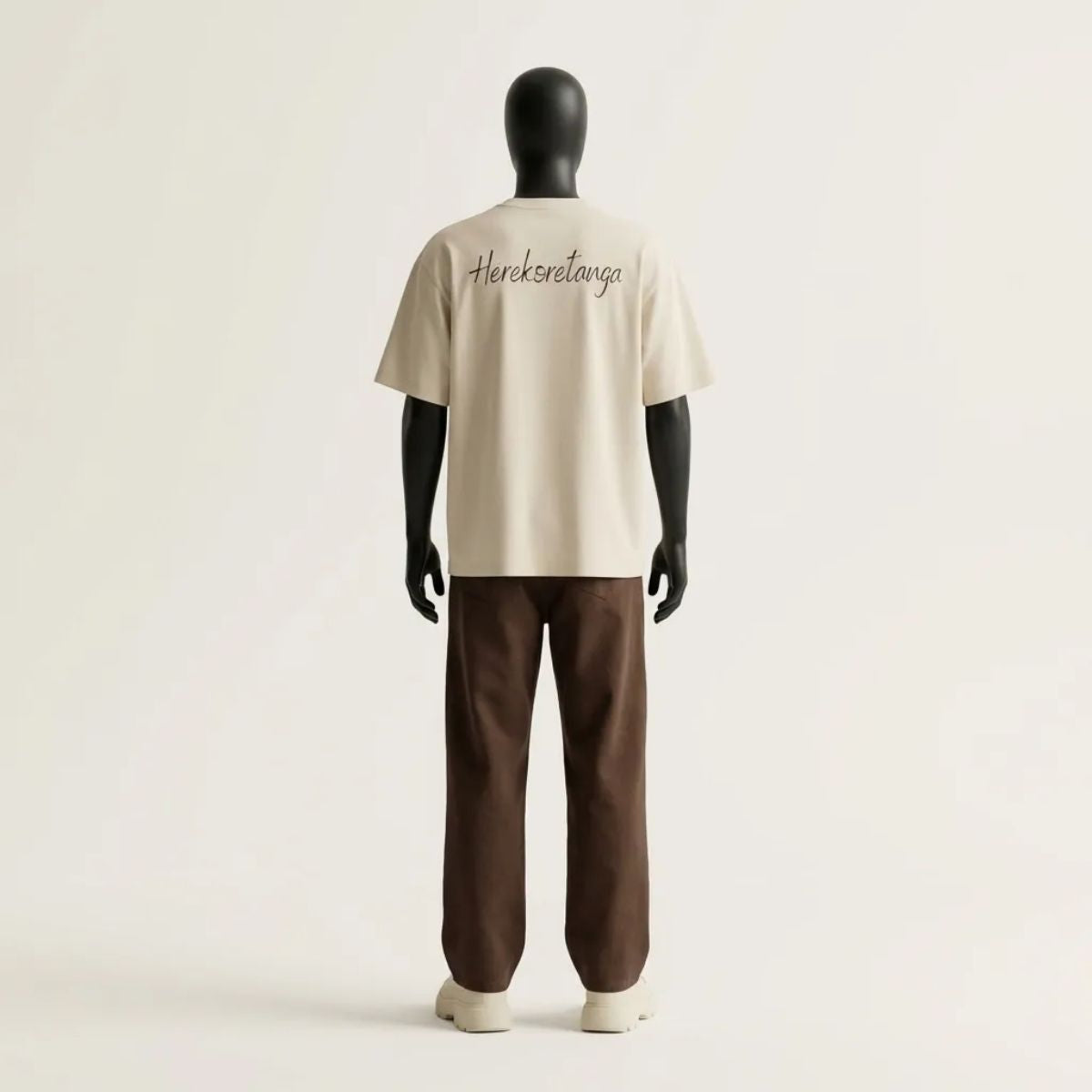 Modulo Herekoretanga: prospettiva posteriore maglia color sabbia 240g/m² su manichino tecnico nero. Studio del volume boxy con grafica "Herekoretanga" ispirato al rigore di Oceania e alla forza della cultura Maori. Architettura tessile GL MANIFACTORY.