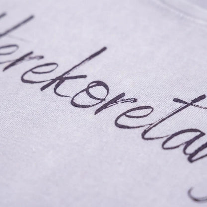 Dettaglio macro della stampa "Herekoretanga" su cotone lilla tenue. Il close-up esalta la trama del tessuto heavy-duty e la precisione della calligrafia, pilastri del design narrativo GL MANIFACTORY.